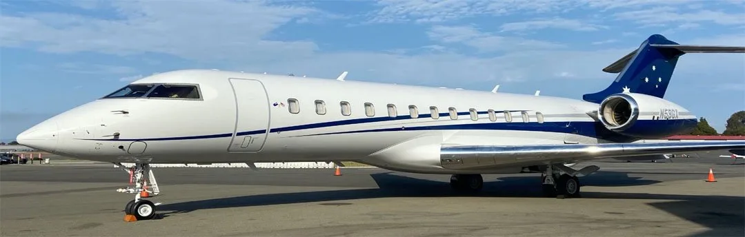 A white and blue Bombardier Challenger 605, N59GX, is parked on an airport tarmac under a blue sky.