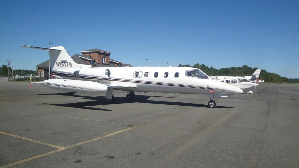 A white Learjet N251TS is parked on an airport tarmac, viewed from the left side.