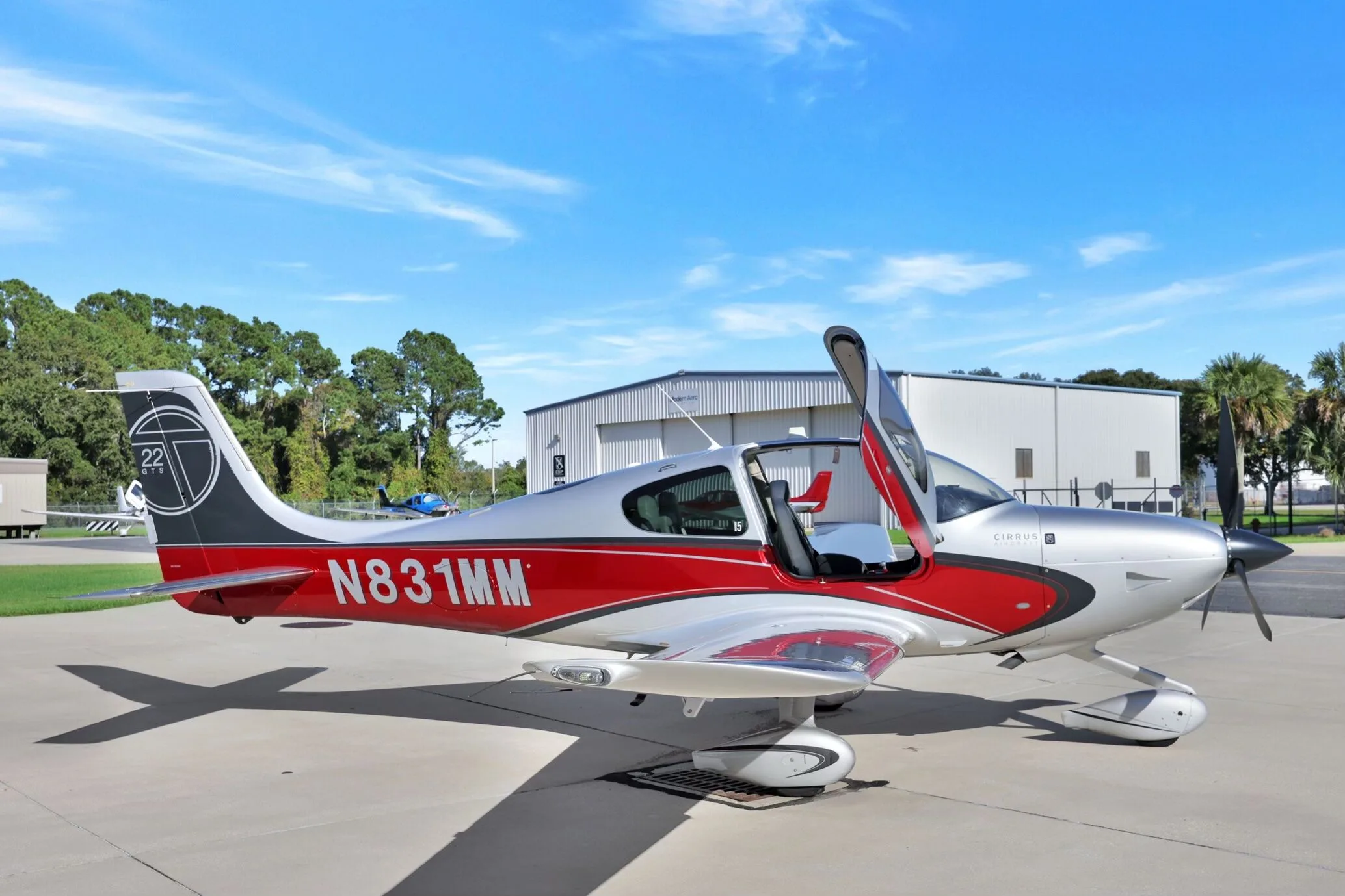 A Cirrus SR22T aircraft with red and silver paint scheme, registration N831MM, parked on an airfield with doors open.