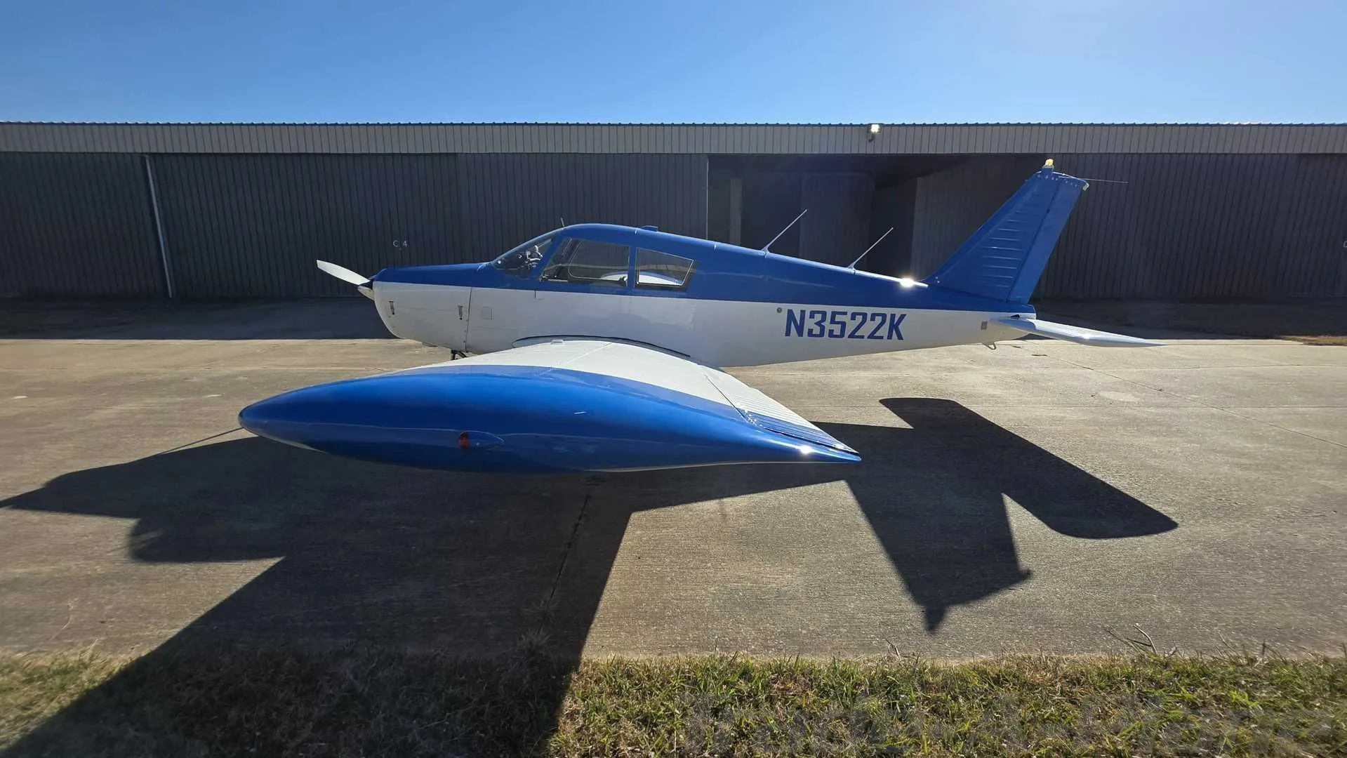 A side view of the blue and white single-engine aircraft, N3522K, parked on an asphalt ramp.