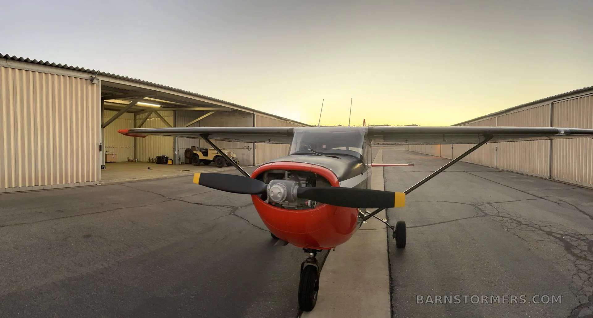 A black, white, and red U.S. Army T-41B aircraft is parked head-on between two hangars at sunset.