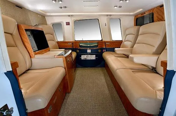 The luxurious interior cabin of a helicopter with tan leather seats facing each other and wood trim.