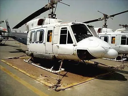 A white utility helicopter, possibly a Bell 212, with its nose cone removed, parked on a tarmac.