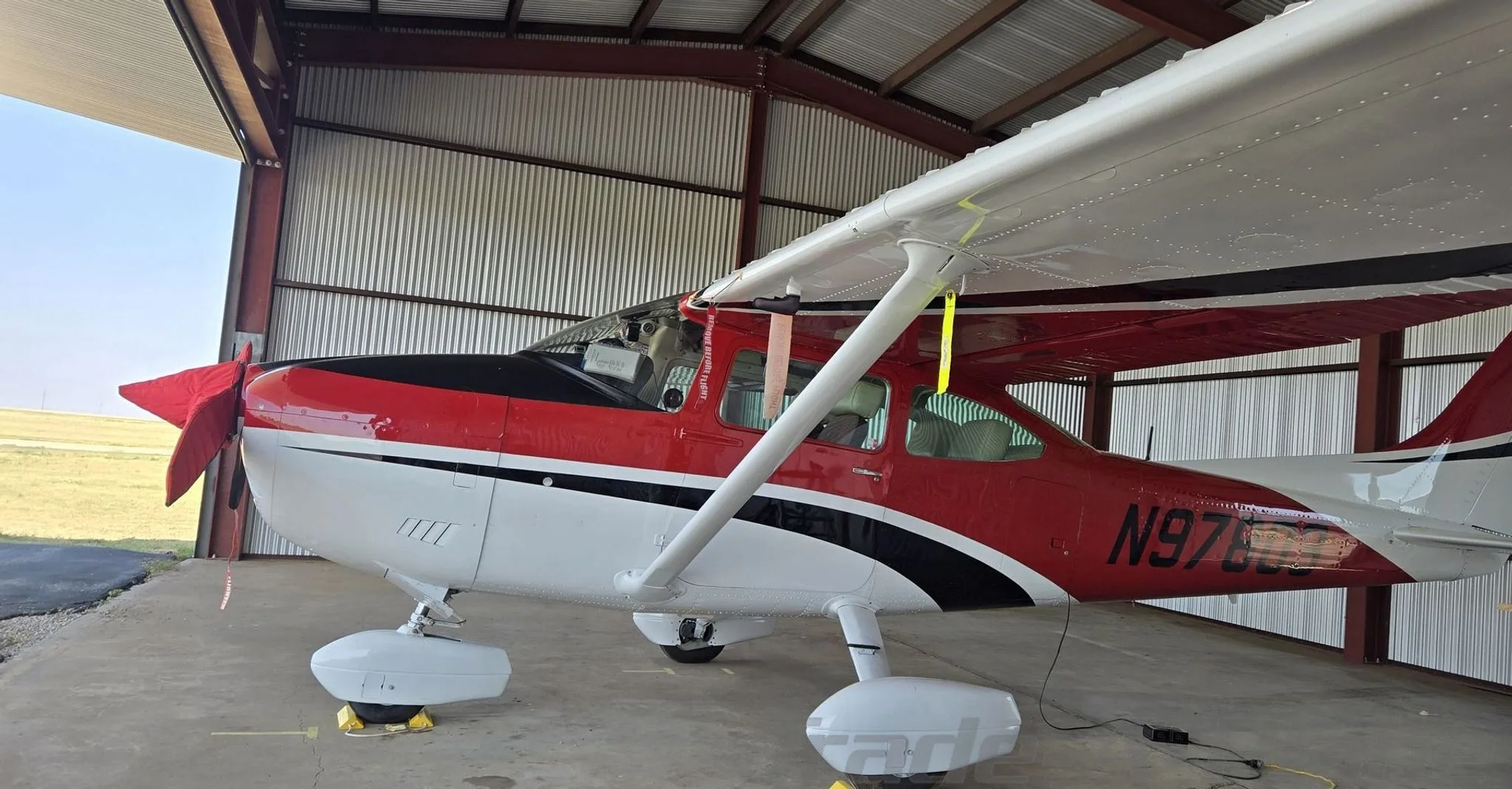 A close-up side view of the red, white, and black Cessna aircraft (N97803) parked inside a hangar.