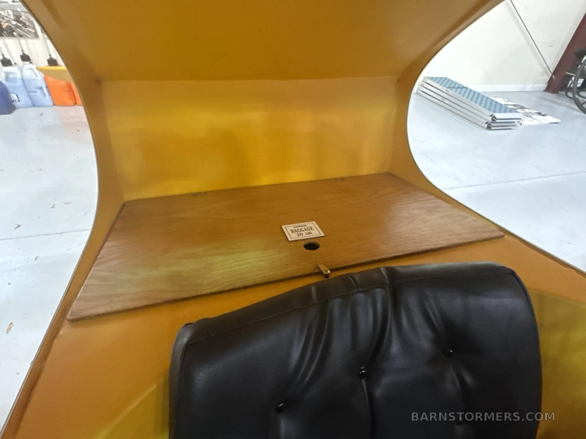 The rear interior of a yellow aircraft showing a black seat and a wooden baggage compartment cover.