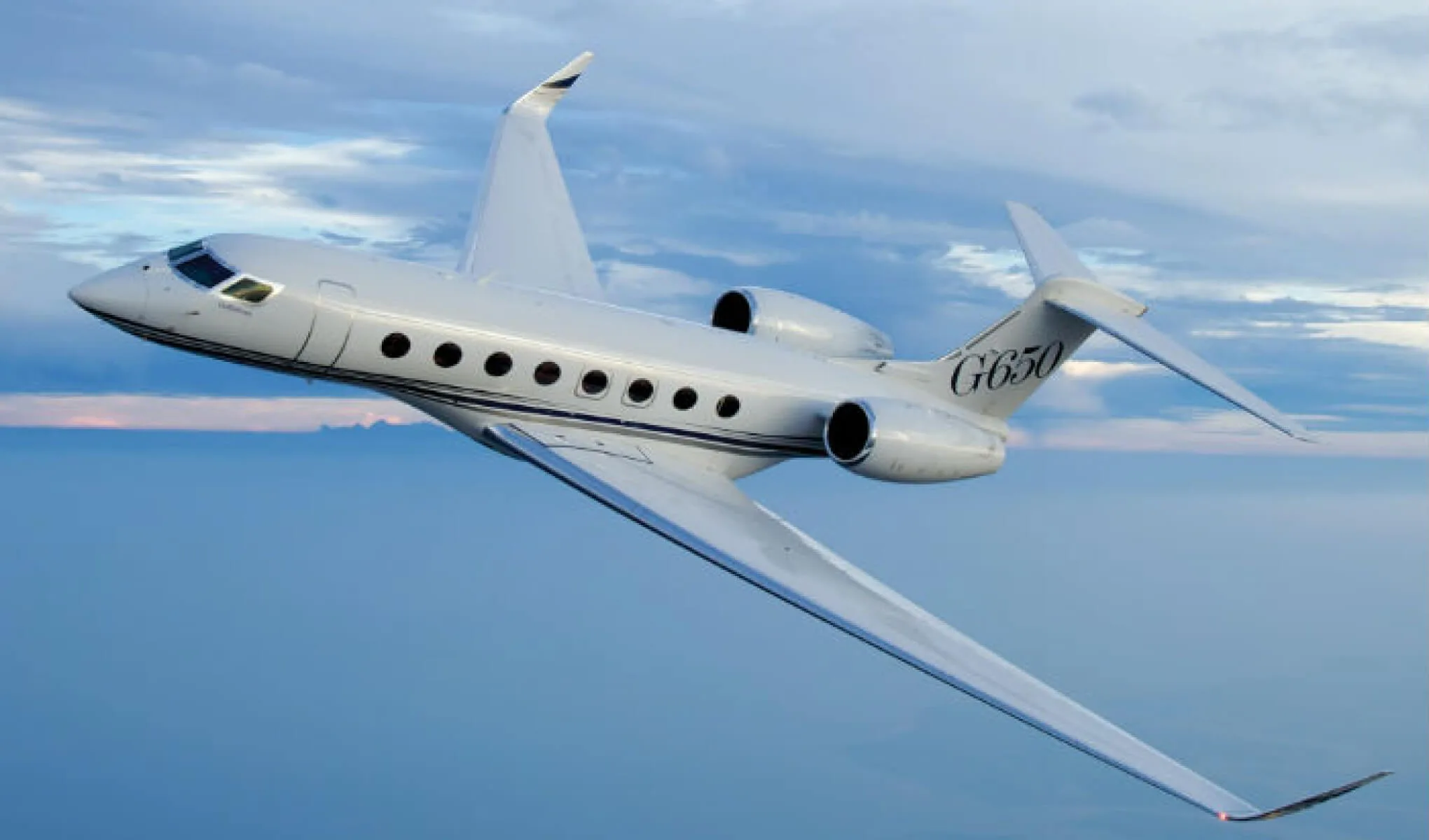 A white Gulfstream G650 business jet with blue pinstripes flying against a cloudy blue sky.