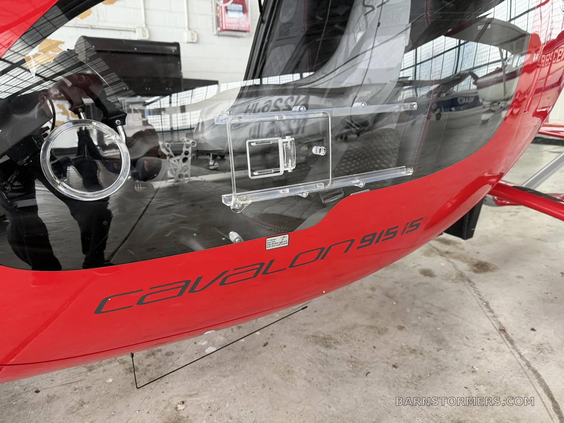 A close-up of the red fuselage of an AutoGyro Cavalon 915iS, showing the model name and a clear window.