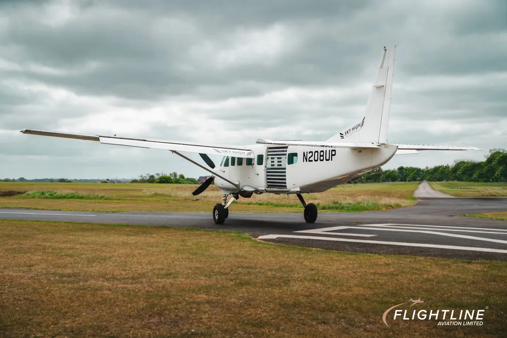 Rear-side view of a white Cessna 208 Caravan with N208UP registration and open cabin door.