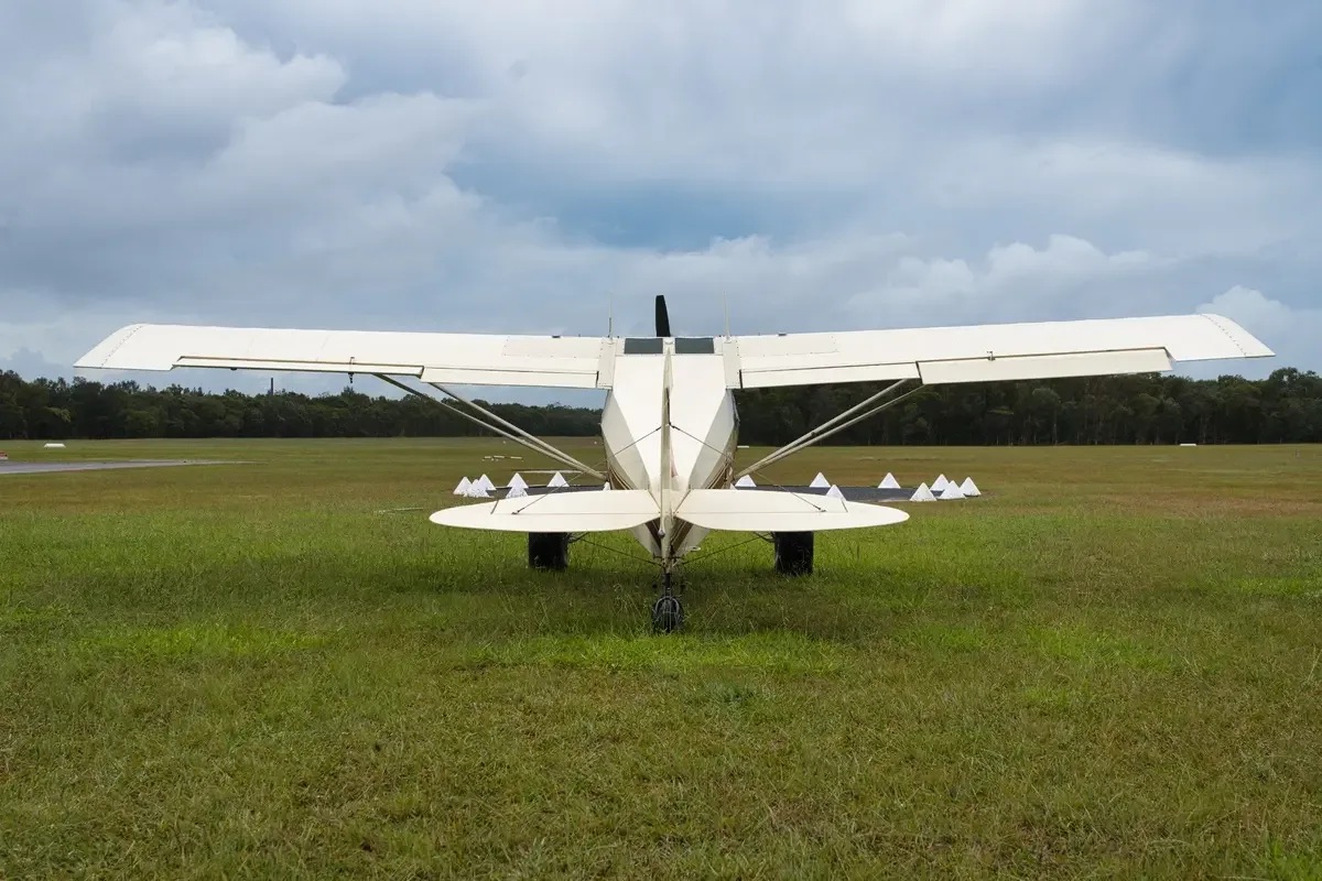 A cream and maroon single-engine taildragger aircraft with registration VH-TSY parked on a grassy airfield, viewed from the rear.