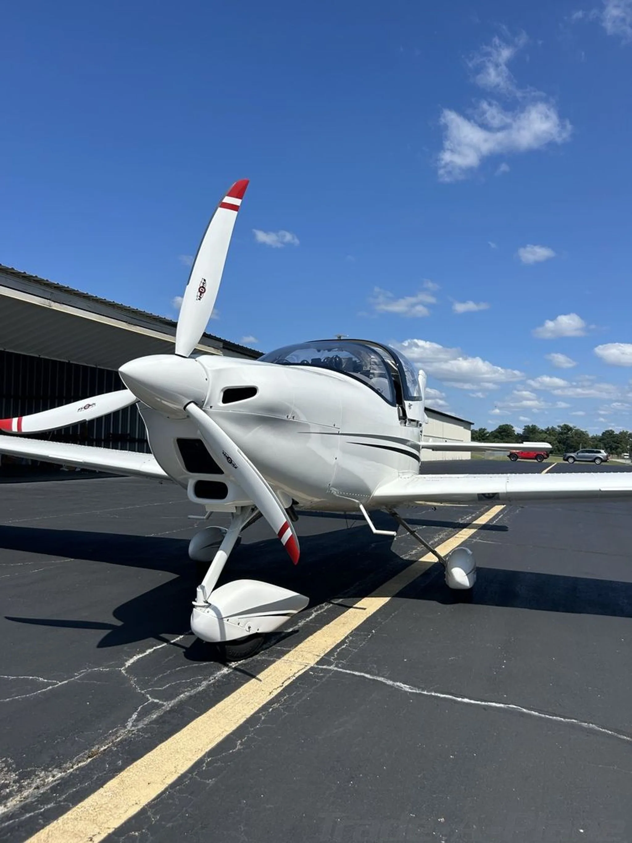 A white Tecnam P2002 Sierra aircraft with red-tipped propeller on an asphalt ramp under a blue sky.