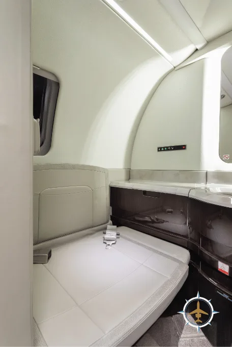 A light-colored leather bench seat with a seatbelt in an aircraft cabin, next to a dark wood-paneled cabinet.