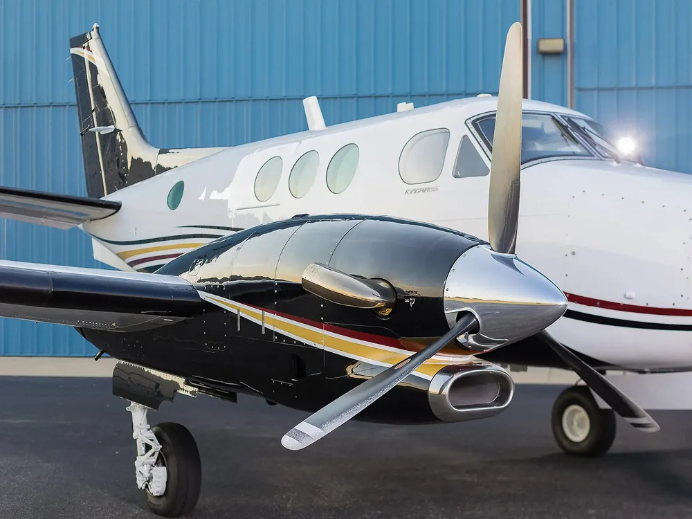 A close-up view of the propeller and front fuselage of a white and black Beechcraft King Air aircraft.