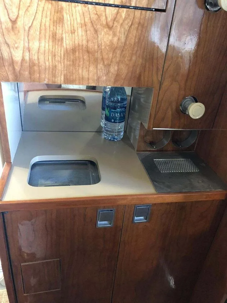 A close-up view of the aircraft's galley area with wooden cabinetry, a small sink, and two bottles of water.