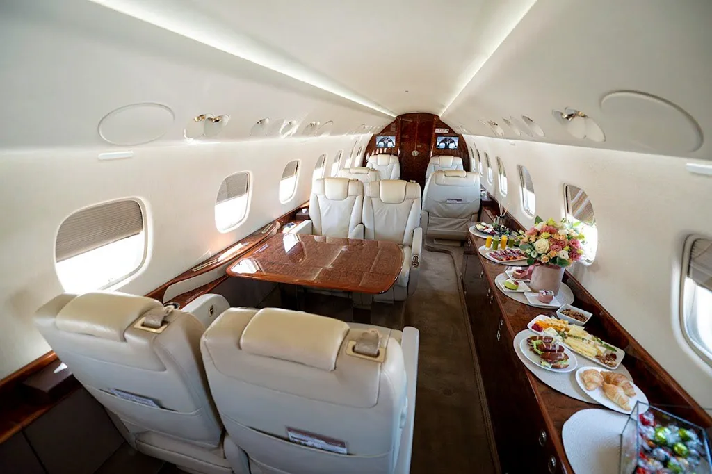 The luxurious cabin interior of a business jet featuring beige leather seats, a polished wooden table, and a spread of food and drinks.