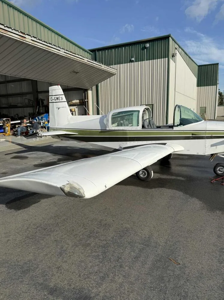 Close-up side view of the fuselage and wing of a white and green Grumman American AA-5 Traveler aircraft with registration C-GWES.