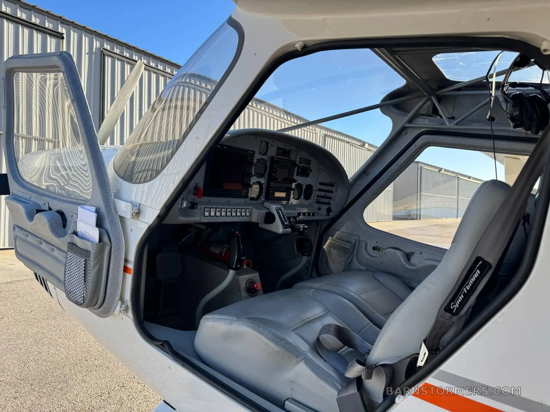 The light gray interior of a small aircraft cabin with an open door, showing front seats and part of the instrument panel.