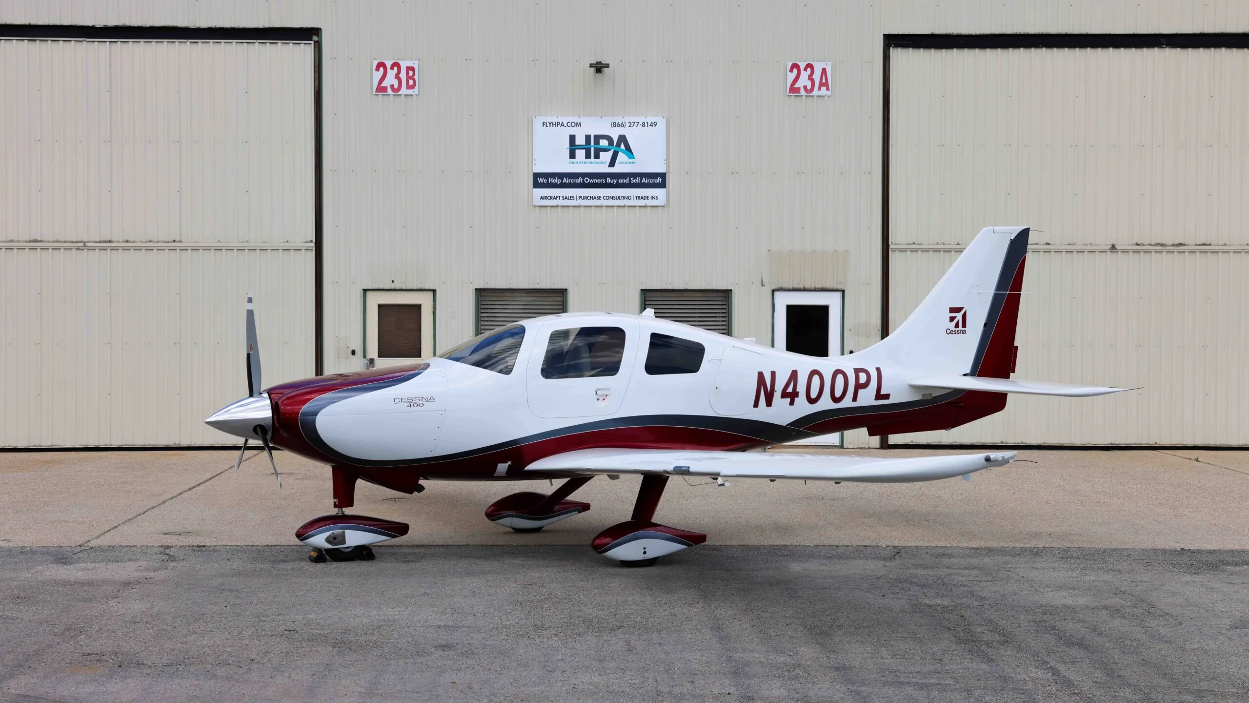 A white and red Cessna 400 aircraft, N400PL, parked in front of hangars.