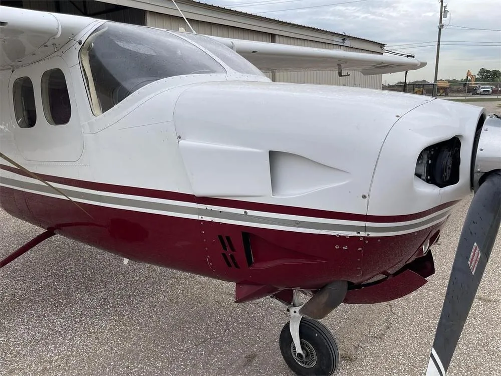 A close-up view of the nose and propeller of a white and maroon Cessna P210 aircraft.
