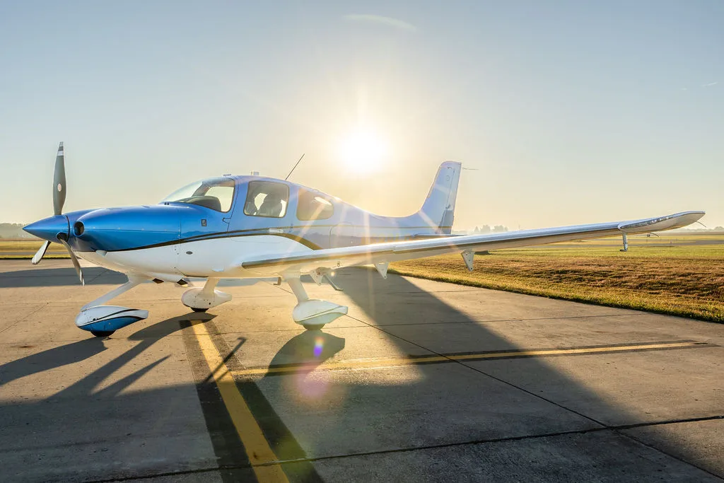 A side view of a blue and white Cirrus SR22 aircraft parked on an airfield with sun flare.