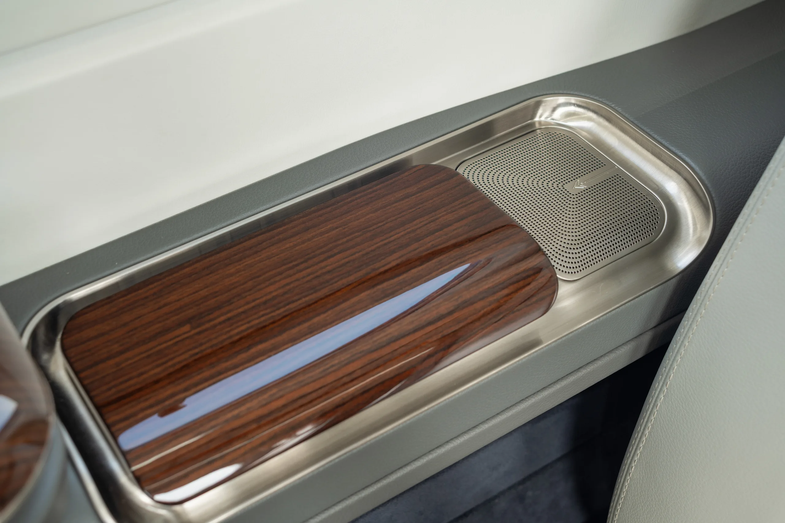 A close-up of an aircraft interior detail showing a polished wood tray and a speaker grille in a side panel.