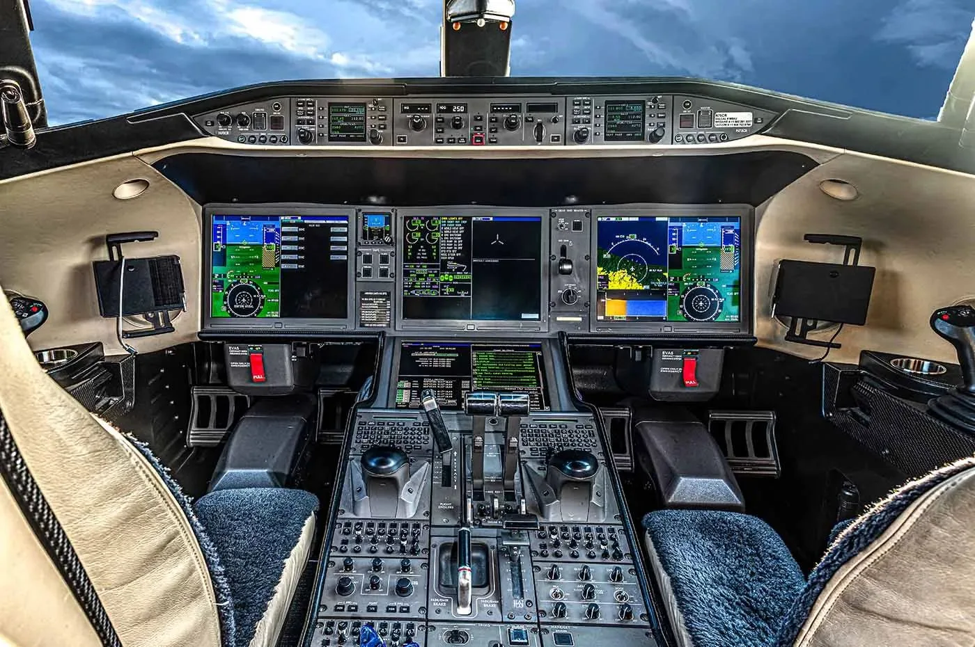 The cockpit of a modern business jet, showing multiple large digital displays and control panels.