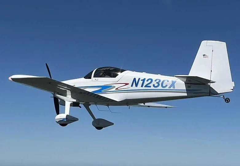 A white N123CX aircraft with blue and gray stripes in flight against a clear blue sky.