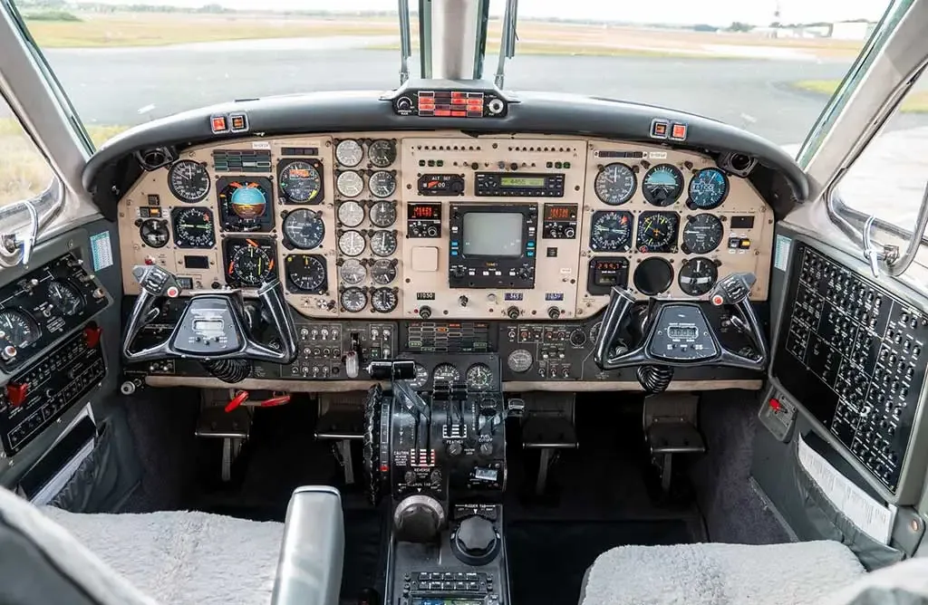 The cockpit of a twin-turboprop aircraft, showing a complex array of analog gauges and a central digital display.