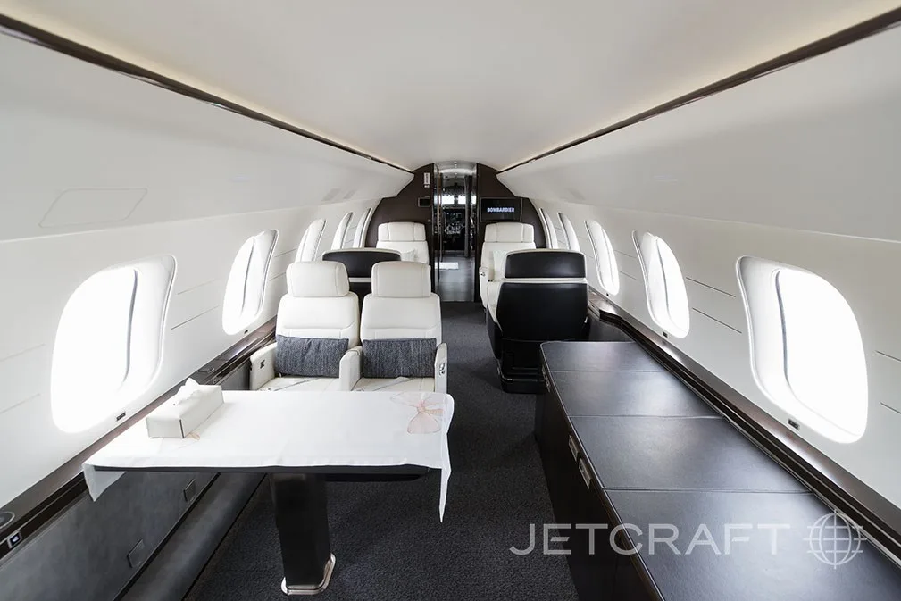 A private jet cabin with a table set for dining and a view towards the rear seating area.