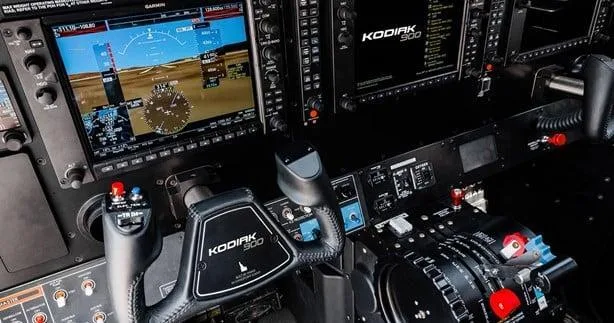 The modern glass cockpit of a Kodiak 900 aircraft, showing multiple digital displays and control yokes.