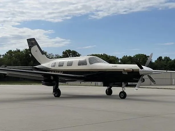 A black and white Piper M-Class aircraft, N522MK, is parked on an airfield tarmac with trees in the background.