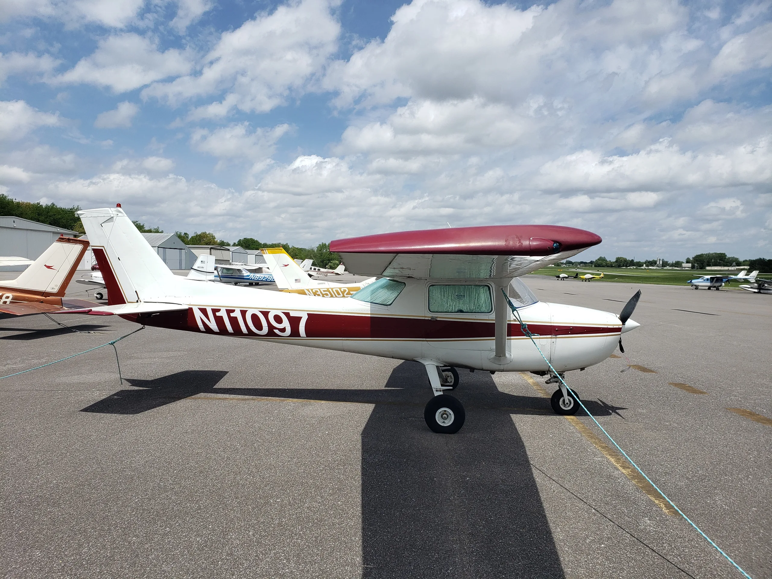 A white and maroon Cessna 150 or 152 aircraft, N11097, parked on an asphalt ramp under a cloudy sky.