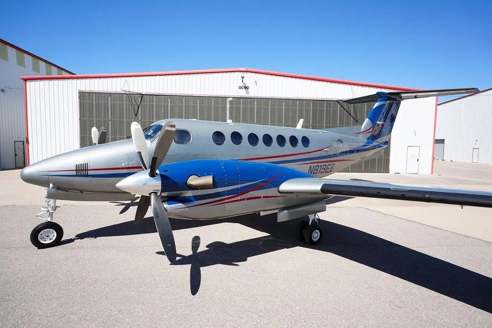 A close-up side view of the silver and blue twin-turboprop aircraft N819EE, parked on an tarmac.
