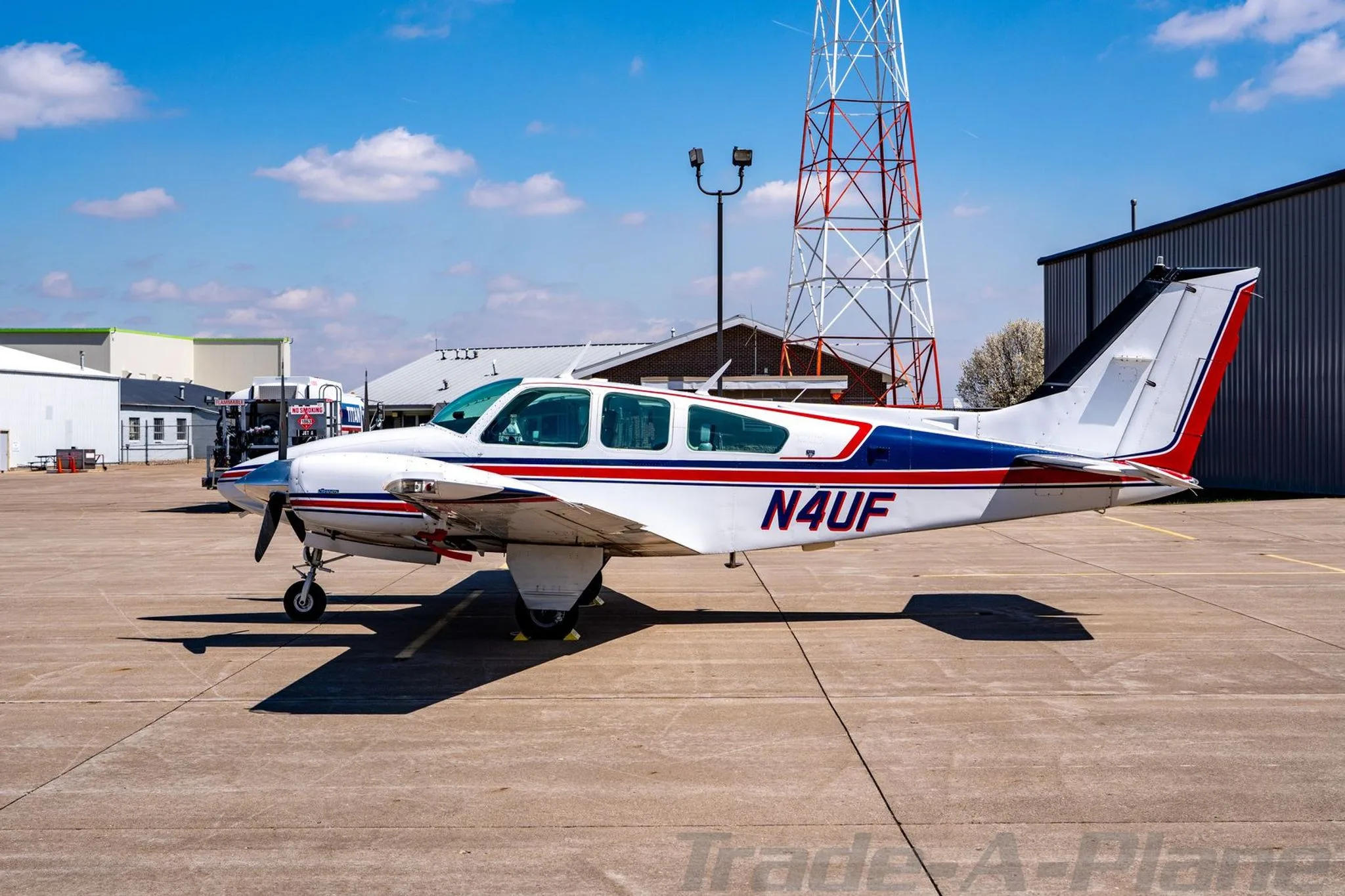Side view of the N4UF twin-engine Beechcraft Baron with red and blue stripes, parked near a radio tower.