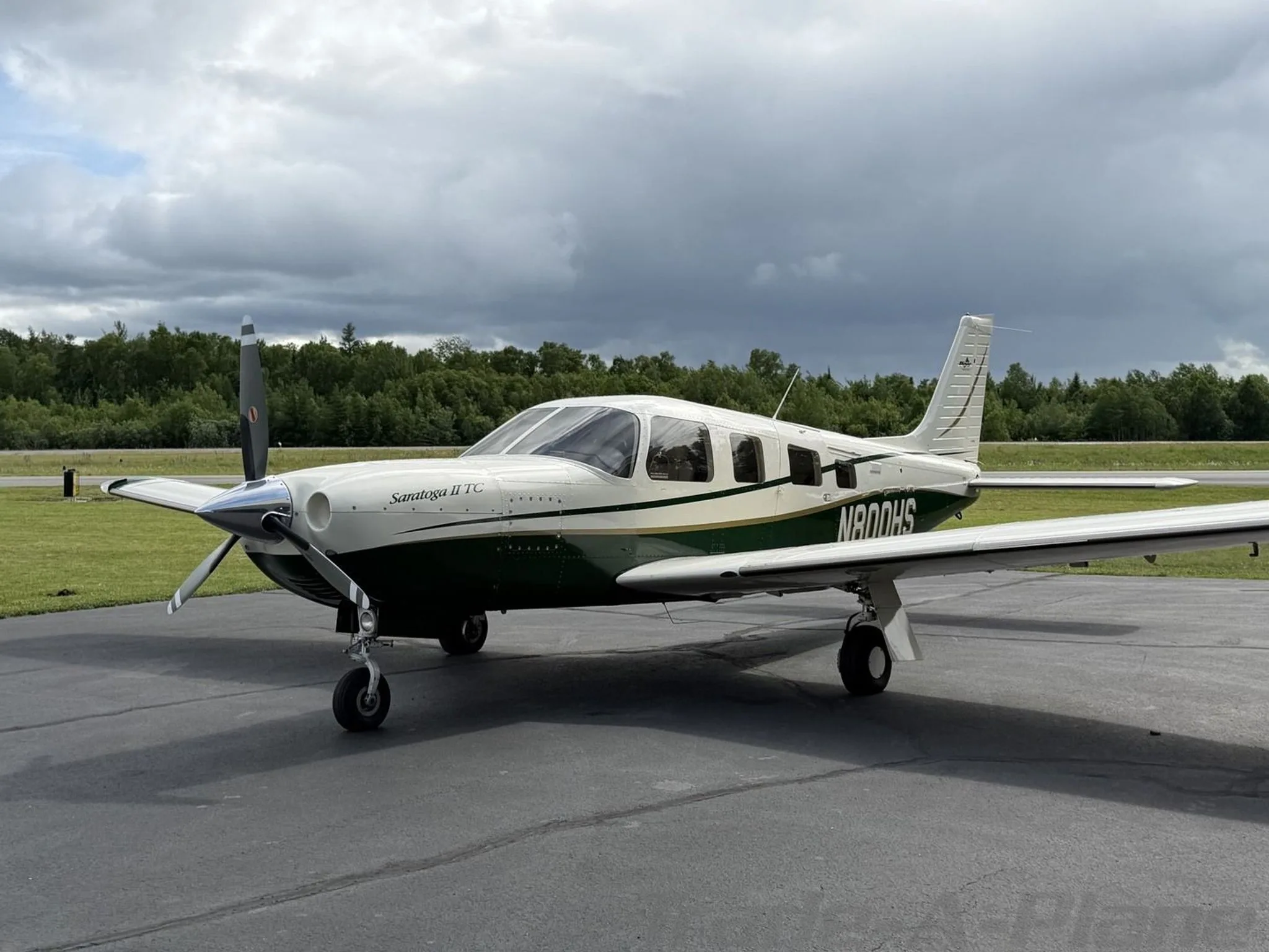 A white and green Piper Saratoga II TC aircraft, registration N800HS, parked on an asphalt ramp under a cloudy sky.