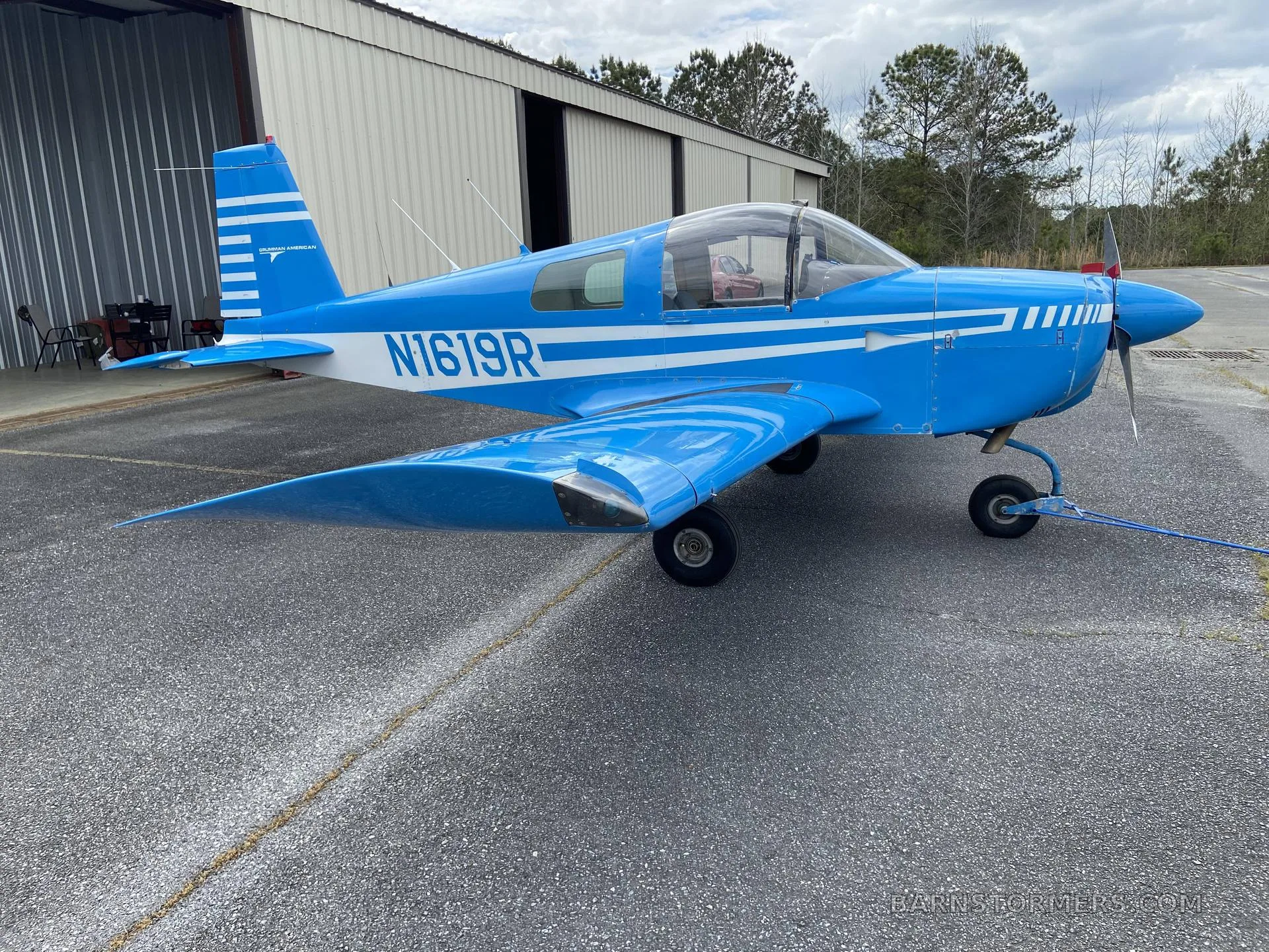 A blue Grumman American aircraft (N1619R) with white stripes parked on the tarmac, viewed from the front-left.