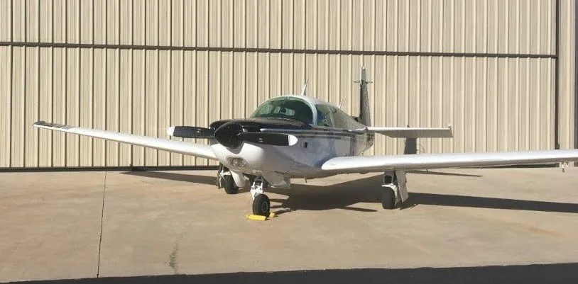 Front view of a white and black Grumman American AA-5 Traveler aircraft, N1047A, parked on concrete.