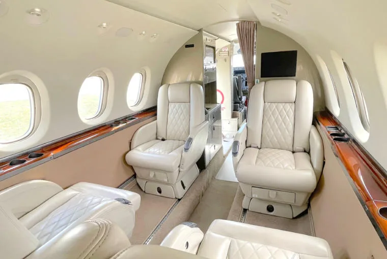 The aircraft's interior cabin with light-colored quilted leather seats and a mounted display screen.