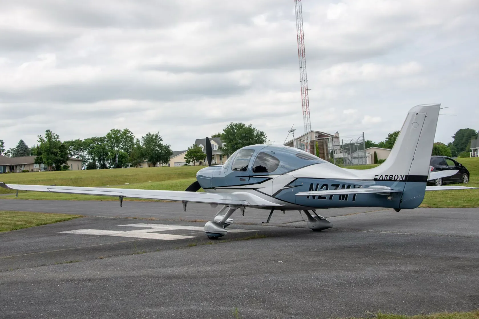 Three-quarter rear view of a blue and white Cirrus SR22T Carbon aircraft, N27MY, on a runway.