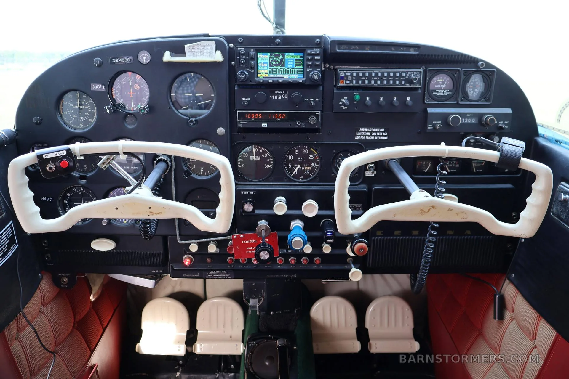 The cockpit of a small aircraft features a black instrument panel with various gauges, radios, and two white control yokes.