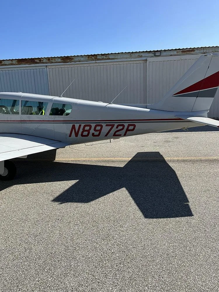 A close-up side view of the tail section of the white Piper Cherokee 180 (N8972P) with red and grey stripes.