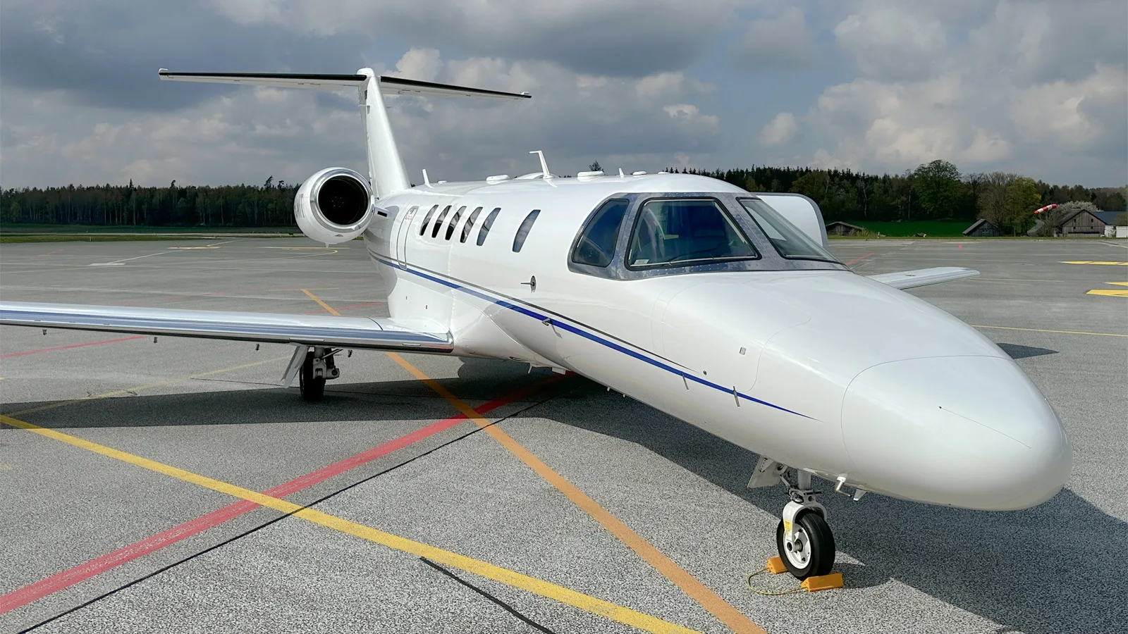 A front-quarter view of a white Cessna Citation CJ4 business jet with blue stripes parked on the tarmac.