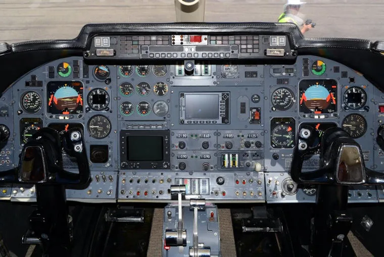 The cockpit of a business jet, featuring a complex instrument panel with multiple screens and analog gauges.