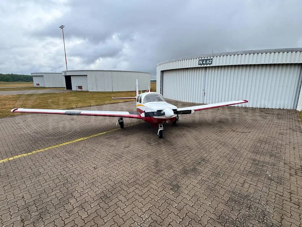 A white and red single-engine aircraft, N880RA, viewed from the front on a paved tarmac with hangars in the background.