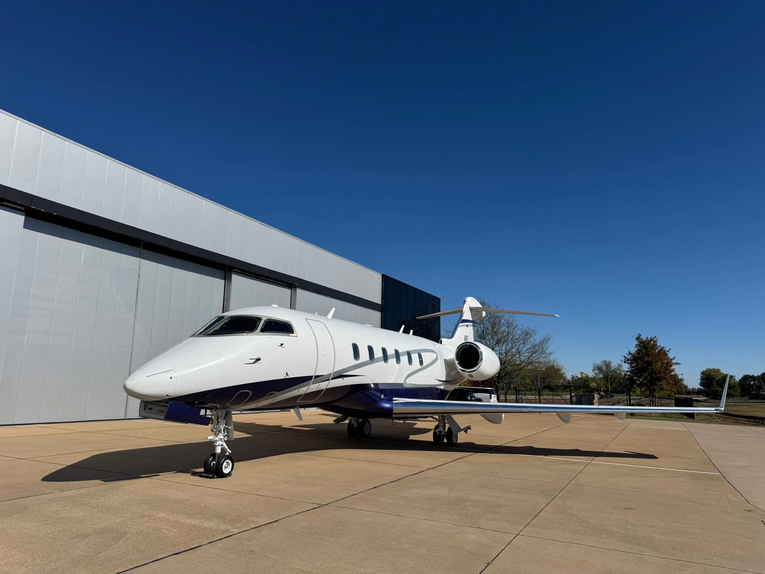 Front-side view of the N5L business jet, a white aircraft with blue and silver stripes, parked on an airfield under a clear blue sky.