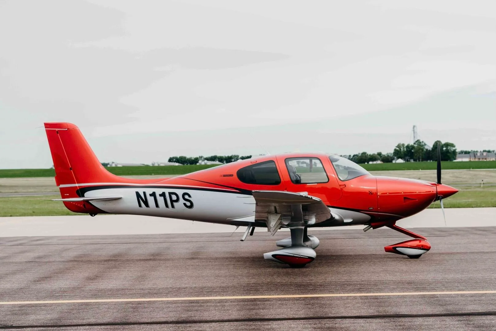 A red and silver Cirrus SR20 Premium aircraft (N11PS) parked on an airfield tarmac.