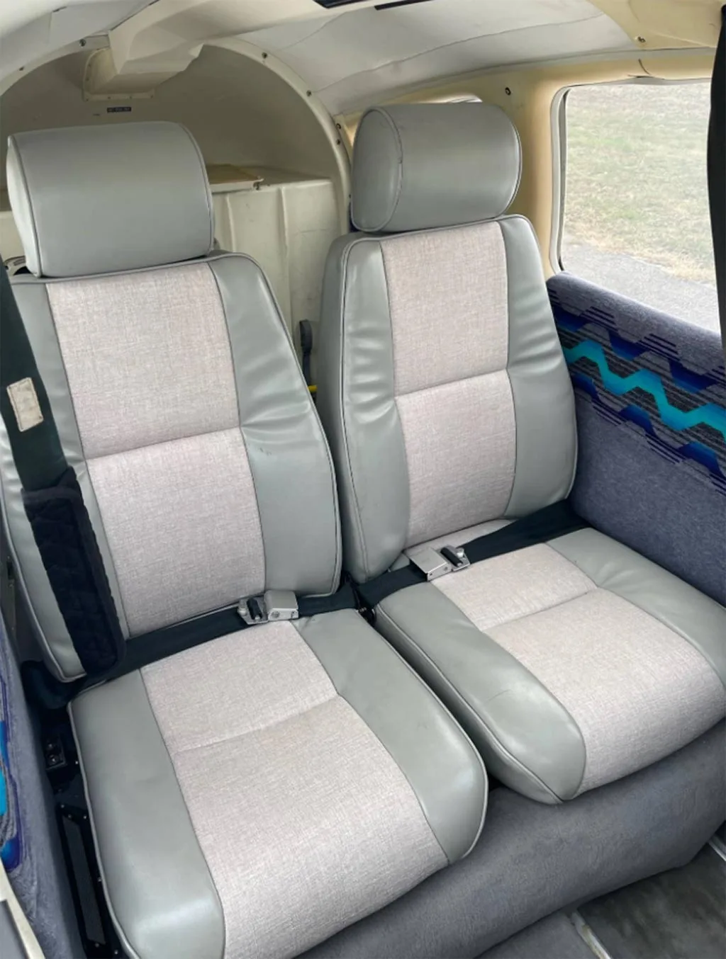 Two light gray and beige passenger seats in the aircraft cabin, with a patterned side panel.