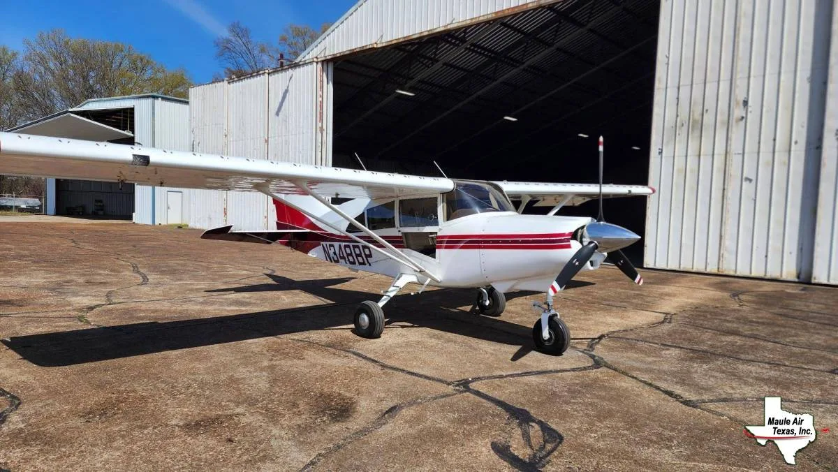 A white and red high-wing single-engine aircraft, registration N348BP, parked on a concrete apron in front of hangars.