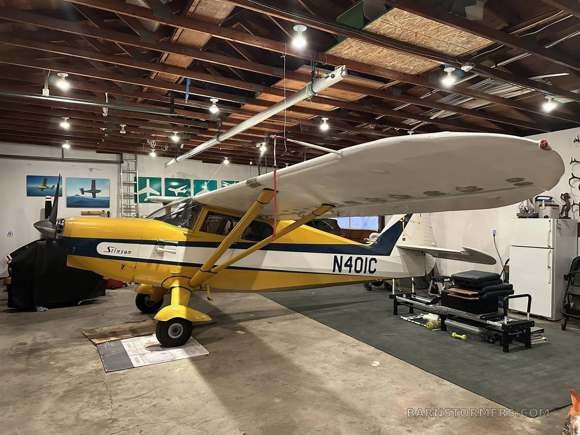 A yellow and blue Stinson aircraft, N401C, parked inside a garage or hangar.