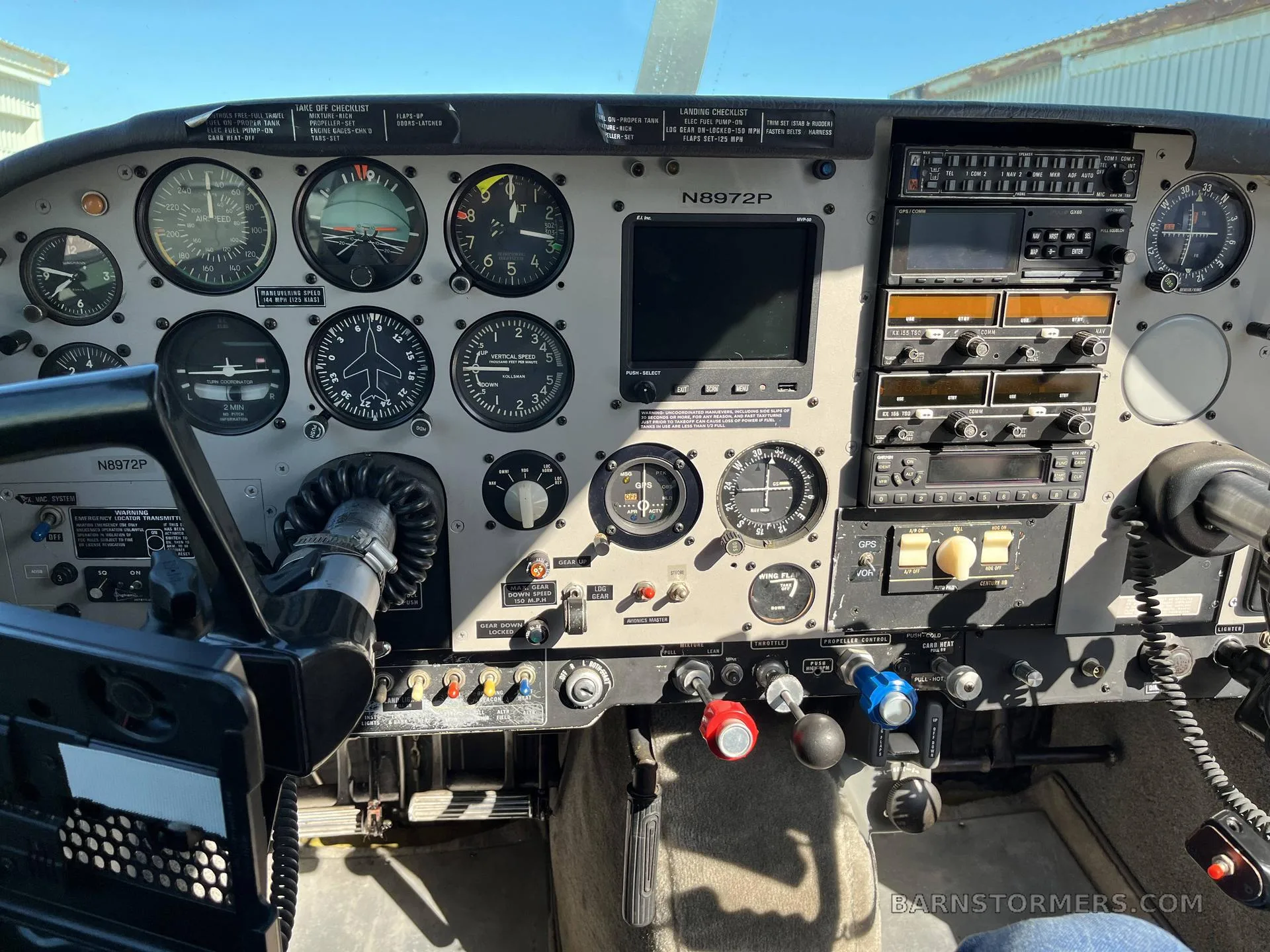 The cockpit of a small aircraft shows the instrument panel with analog gauges, avionics, and a control yoke.