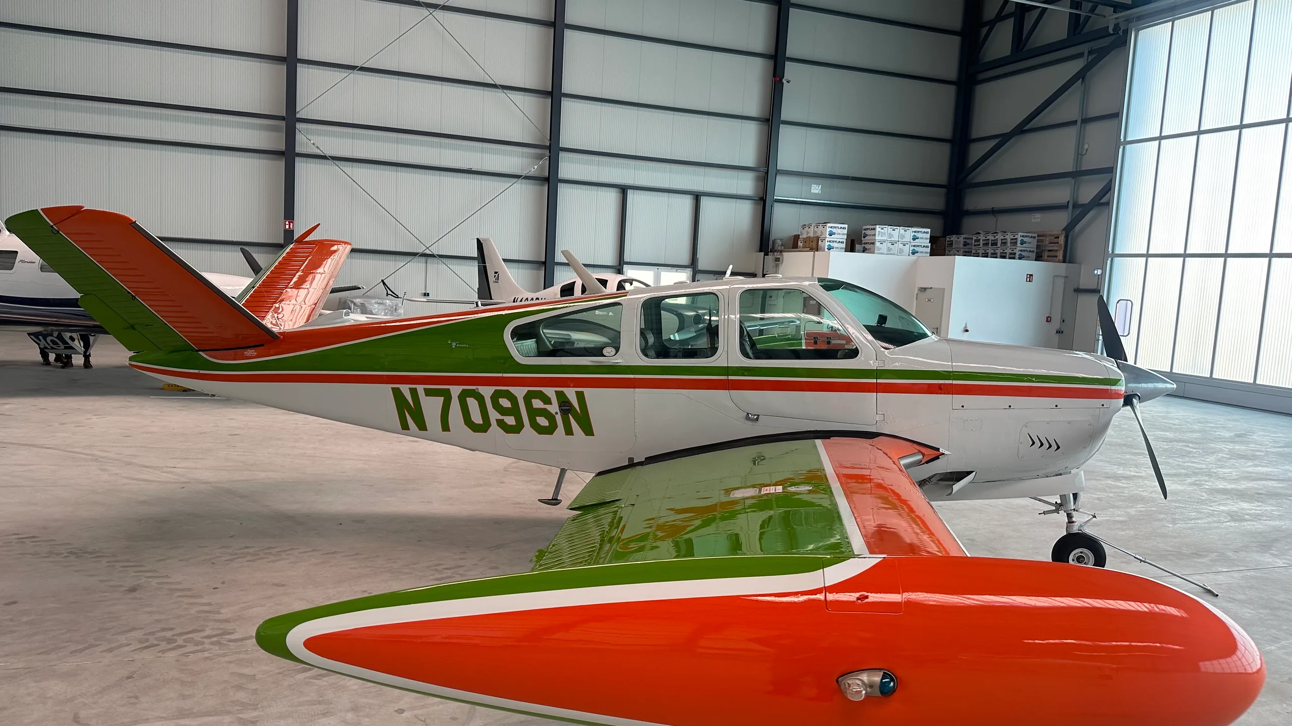 A white single-engine aircraft with green and orange stripes, registration N7096N, parked inside a hangar.